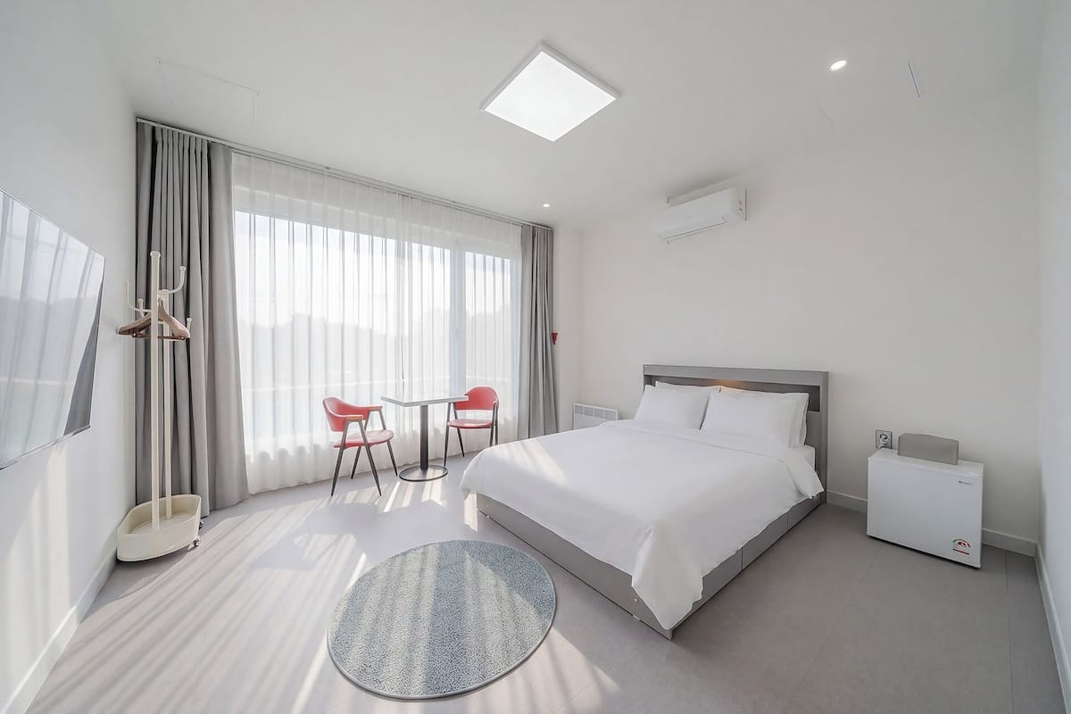 Habitación de hotel con cama, alfombra redonda, mesa con sillas, televisor y ventana con cortinas.
