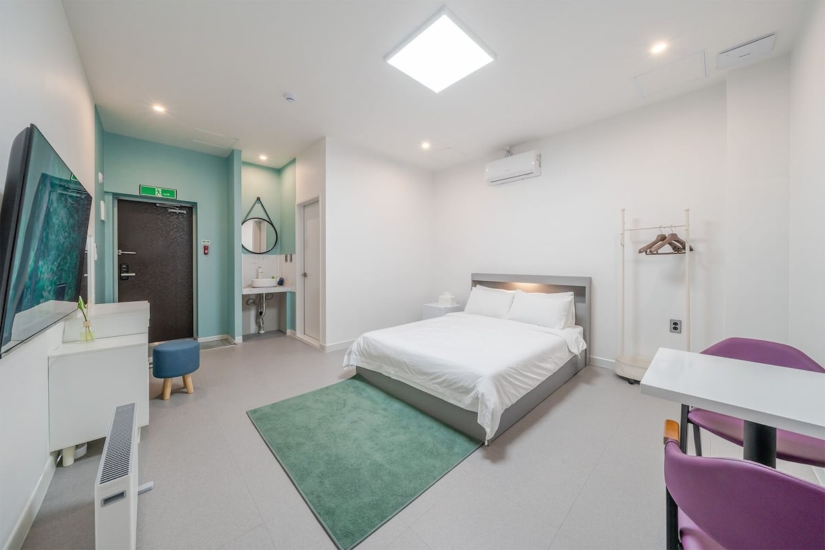 Habitación de hotel con cama, escritorio, silla, armario, espejo y baño.