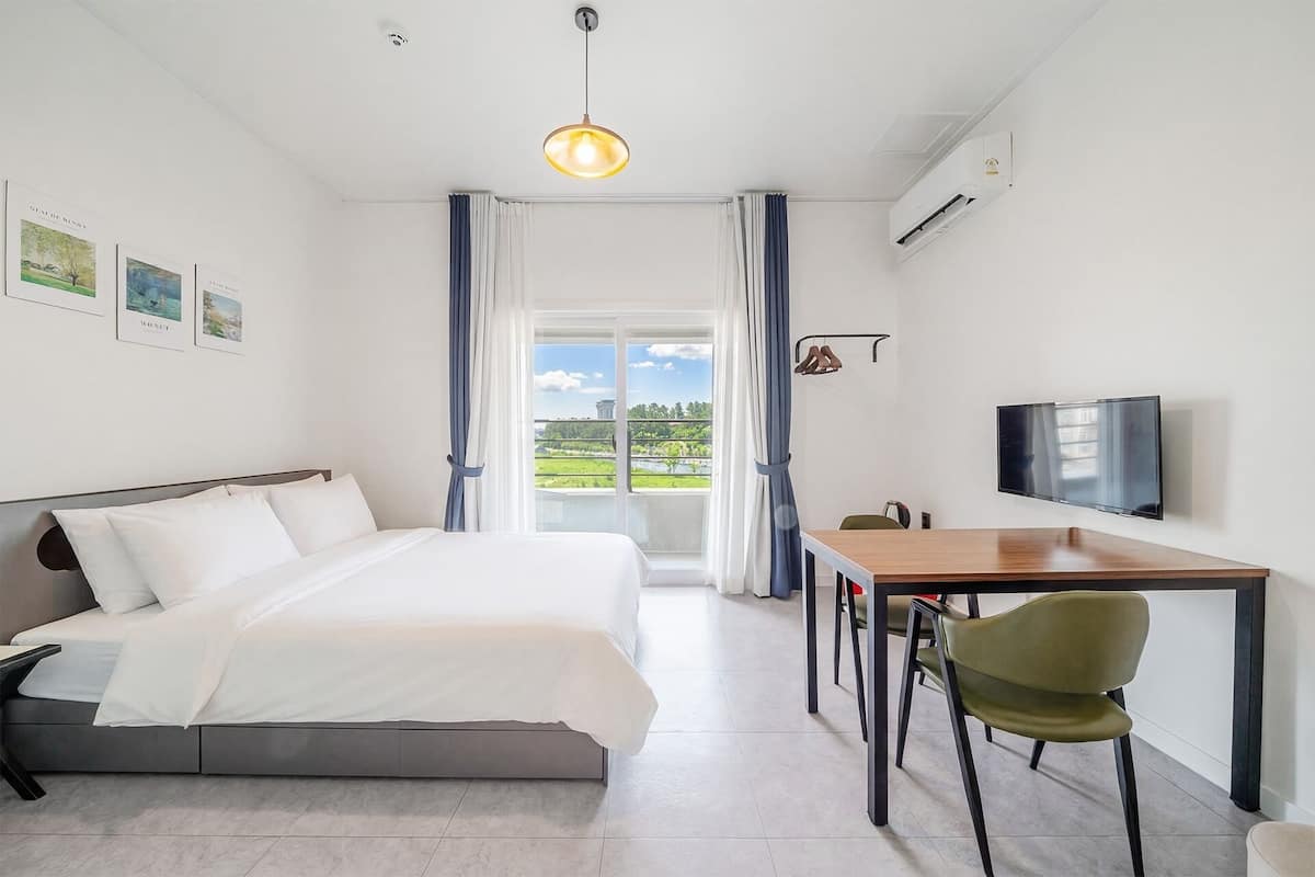 Habitación de hotel con cama, escritorio con silla, televisión y vistas al exterior.