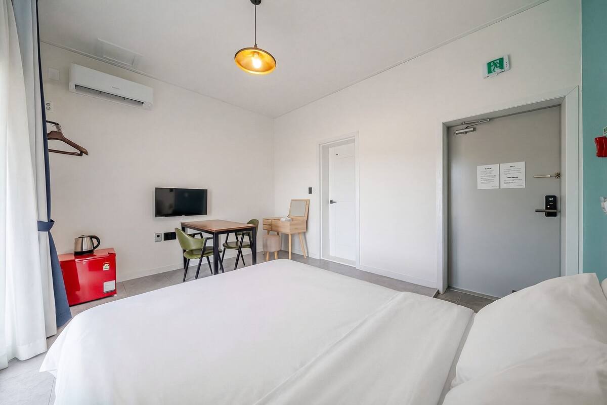 Habitación de hotel con cama, escritorio con silla, televisión y puerta con letrero de salida de emergencia.