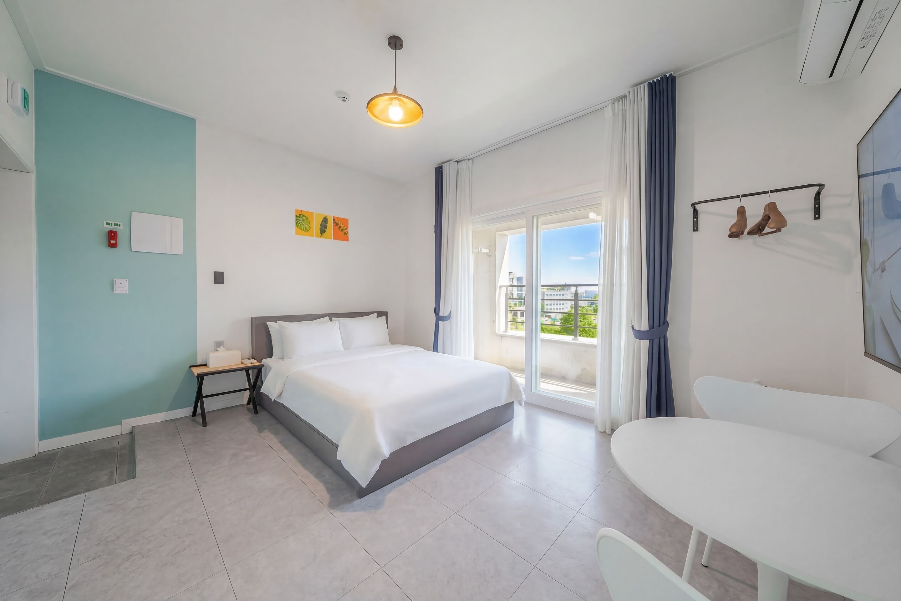 A hotel room with a bed, bedside table, and a view of the outdoors.