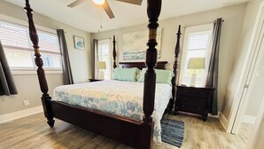 A four-poster bed with a floral bedspread, a ceiling fan, and a nightstand with a lamp. - New Reno 1.3M 2 Beach Full Kit, W&D, Large 2BD 2BA (Bonita Springs)
