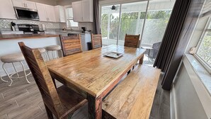 A kitchen with white cabinets, a stainless steel oven, and a dining area with a wooden table and chairs. - New Reno 1.3M 2 Beach Full Kit, W&D, Large 2BD 2BA (Bonita Springs)