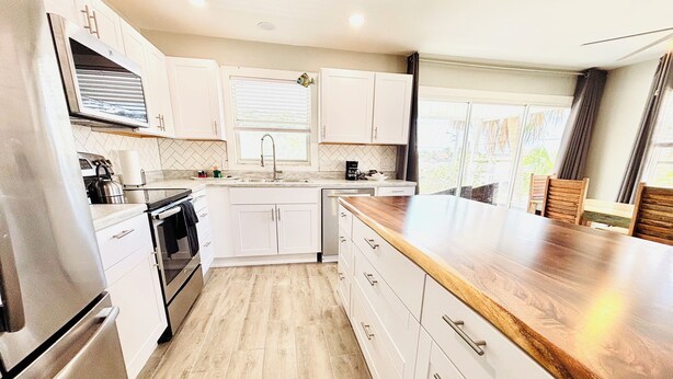 A modern kitchen with white cabinets, a wooden countertop, and a stainless steel refrigerator. - New Reno 1.3M 2 Beach Full Kit, W&D, Large 2BD 2BA (Bonita Springs)