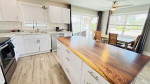 A modern kitchen with white cabinetry, a wooden countertop island, and a dining area with a view. - New Reno 1.3M 2 Beach Full Kit, W&D, Large 2BD 2BA (Bonita Springs)
