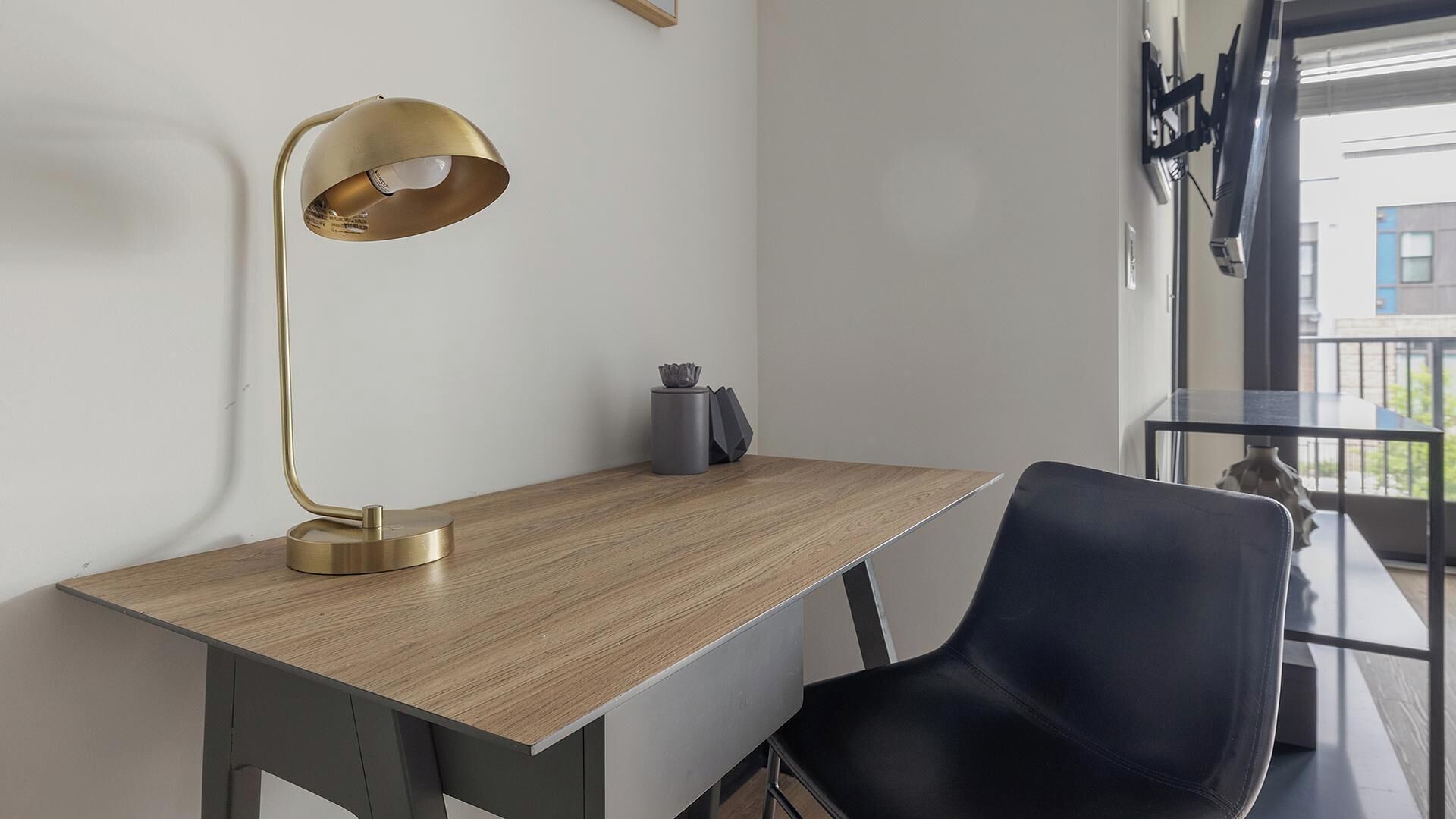 A modern workspace with a wooden desk, a black chair, a gold desk lamp, and a grey vase.
