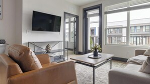 Ett modernt vardagsrum med en soffa i läder, ett soffbord i glas, en platt-TV och utsikt över staden genom stora fönster.