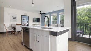 A modern kitchen with a central island, a dining area with a table and chairs, and a large window with a view of trees. - Landing | Chic 2BD, Game Room, Clubhouse (Atlanta)