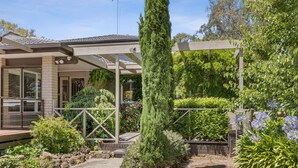 A residential property with a covered patio, a tall coniferous tree, and a variety of shrubs and flowering plants.