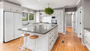 A modern kitchen with white cabinetry, a large island with stools, and a hanging plant.