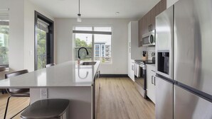 Una cocina moderna con una isla grande, electrodomésticos de acero inoxidable y vistas a un edificio.