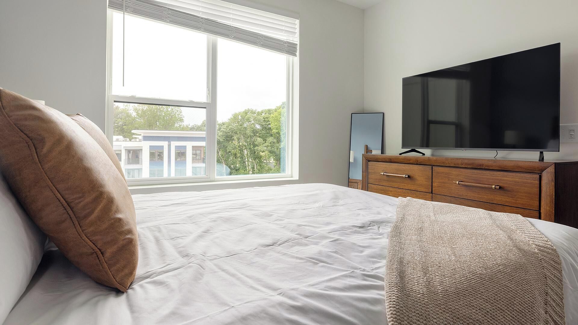 A bedroom with a bed, a dresser, a TV, and a window with blinds.