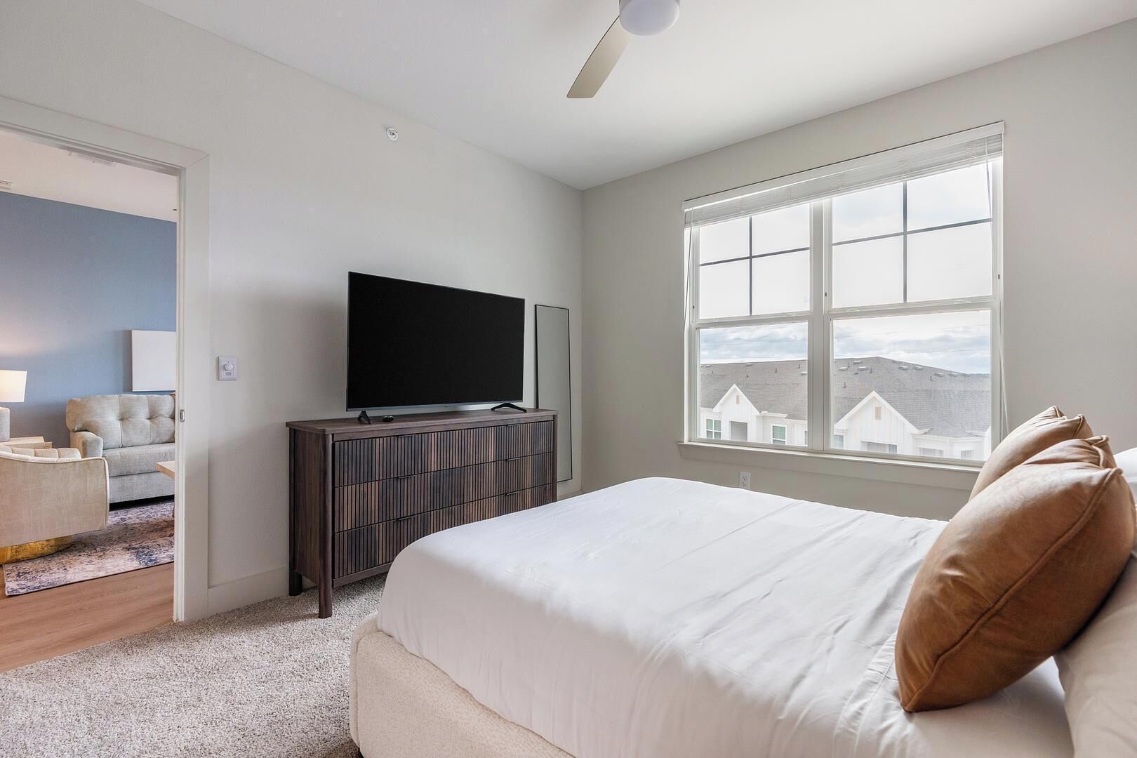 A bedroom with a bed, a TV on a dresser, a window with a view, and a door leading to another room.