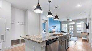 Eine moderne Küche mit Granit-Arbeitsplatten, Edelstahlgeräten, Pendelleuchten und Blick zum Wohnbereich.