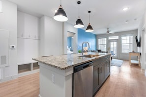 Eine moderne Küche mit Granit-Arbeitsplatten, Edelstahlgeräten, Pendelleuchten und Blick zum Wohnbereich.