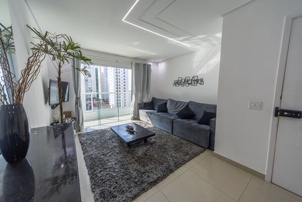 Una sala de estar moderna con un sofá, una mesa de centro, una planta grande y vistas de rascacielos a través de un ventanal.