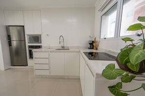 Una cocina moderna con armarios blancos, horno empotrado, microondas y pileta.