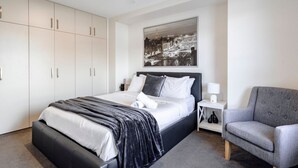 Un dormitorio moderno con cama, una silla, una mesita de noche y un ventilador de techo.