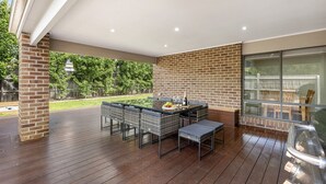 An outdoor patio with a brick wall, wooden flooring, and a table set for dining. - Summer Breeze - 10 mins to Barwon Heads & Torquay! (499552) (Armstrong Creek)