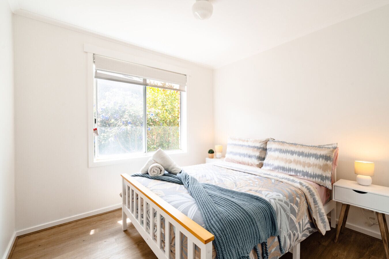 A bedroom with a bed, a window, a bedside table with a lamp, and a small plant.