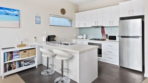 Ett modernt kök med vita skåp, en köksö med barstolar, en inbyggd ugn och ett kylskåp i rostfritt stål.