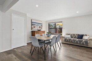 A dining area with a wooden table and chairs, a sofa, and a painting of a beach scene.