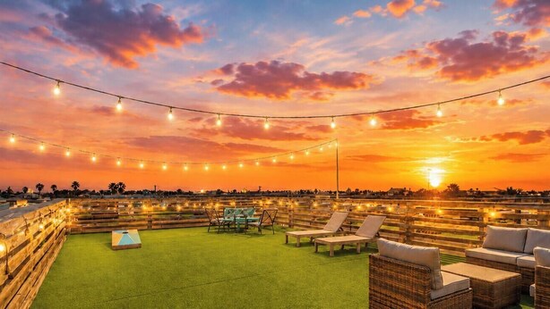 Una terraza en la azotea con luces colgantes, mobiliario exterior y vistas al atardecer.