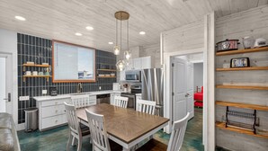 Una cocina moderna con armarios blancos, una mesa de comedor de madera e iluminación colgante.