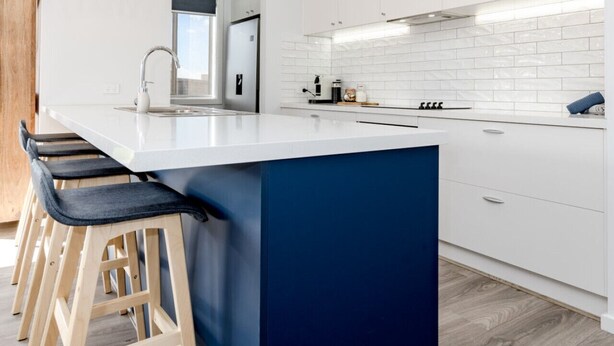 Una cucina moderna con isola centrale, sgabelli da bar, mobili bianchi e lampade a sospensione in rattan.