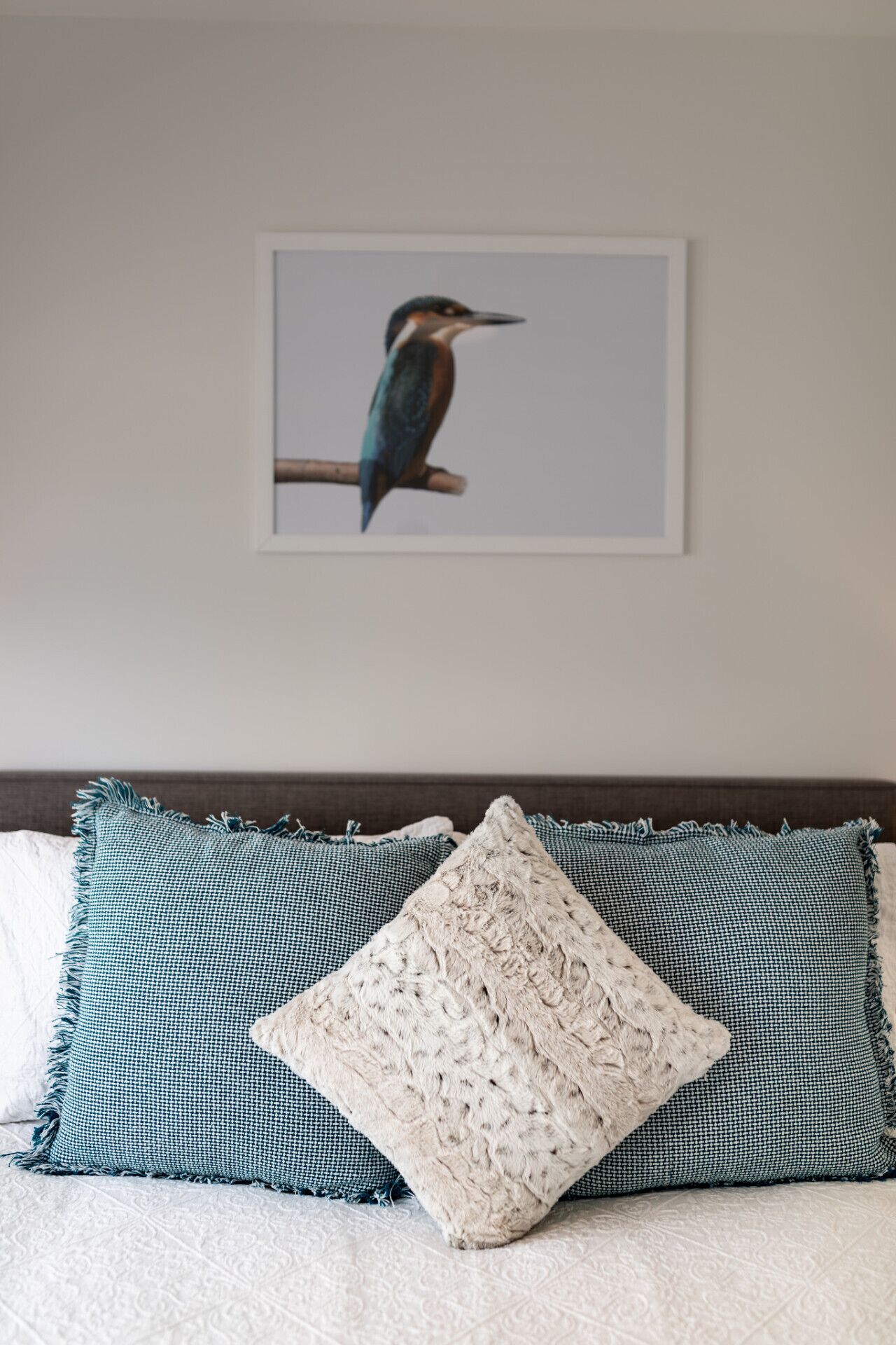 A bed with patterned pillows and a framed bird painting on the wall.