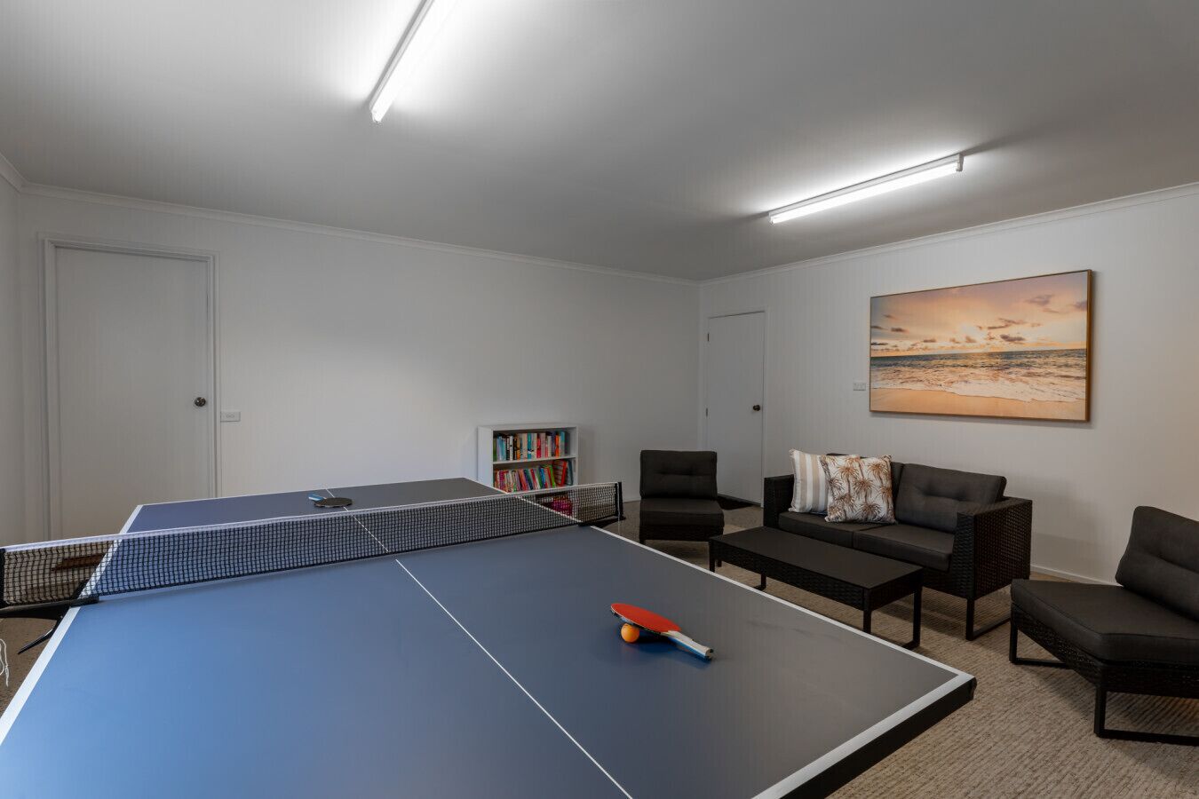 A room with a ping pong table, a bookshelf, and a sofa.