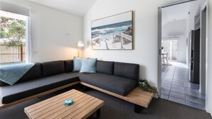 A modern living room with a sectional sofa, a wooden coffee table, a floor lamp, and a coastal landscape painting. - The Grove - Sleeps 6 - Pet Friendly! (499545) (Ocean Grove)