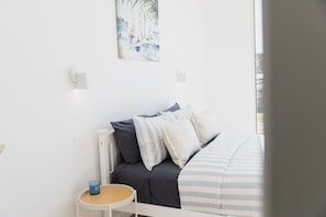 Ein Schlafzimmer mit Bett, Kissen, einem Nachttisch mit Kerze und einem Bild an der Wand.