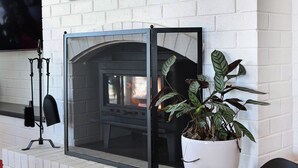Una chimenea de ladrillo blanco con protector, una planta en maceta y un televisor montado en la pared.