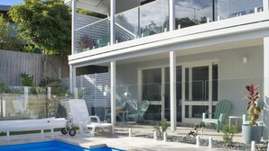 Una casa moderna de dos pisos con piscina, mobiliario exterior y jardín vallado.