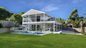 Una casa de dos pisos con un balcón acristalado, una piscina y un césped bien cuidado.