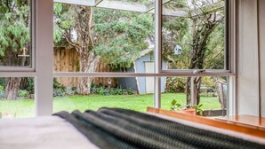 Un dormitorio con un ventanal grande que da a un jardín con árboles y una valla de madera.