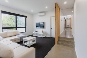 A modern living room with a sofa, coffee table, TV, and a staircase leading to another area. - Greenview Luxe - Sleeps 7 - Firepit! (499541) (Ocean Grove)