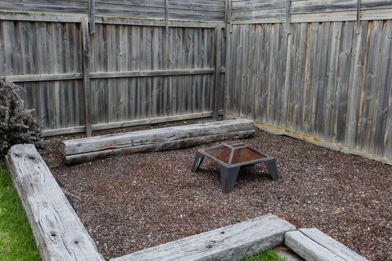 A fenced backyard with a small wooden table and steps leading to a raised platform.