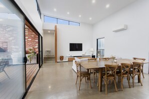 A modern interior with a dining area, a TV mounted on the wall, and a view of the outdoors. - Greenview Luxe - Sleeps 7 - Firepit! (499541) (Ocean Grove)