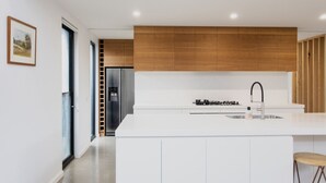 Une cuisine moderne avec des meubles blancs, un réfrigérateur en acier inoxydable, une cuisinière à gaz et un mur d’accent en bois.
