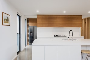 A modern kitchen with white cabinetry, a stainless steel refrigerator, a gas stove, and a wooden accent wall. - Greenview Luxe - Sleeps 7 - Firepit! (499541) (Ocean Grove)