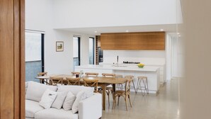 Une cuisine moderne avec des meubles blancs, un îlot central et un coin repas doté de meubles en bois.