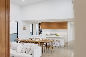A modern kitchen with white cabinetry, a central island, and a dining area with wooden furniture. - Greenview Luxe - Sleeps 7 - Firepit! (499541) (Ocean Grove)