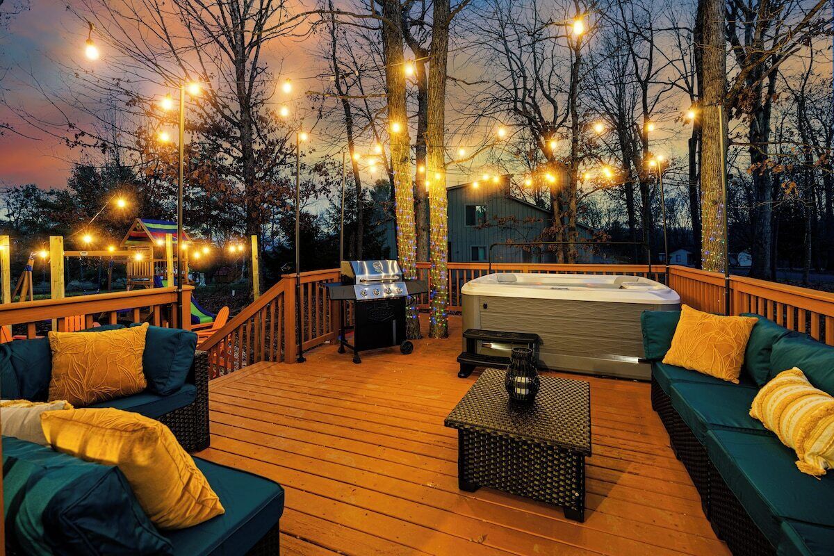 A wooden deck with outdoor seating, a hot tub, and string lights.