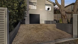 Une maison moderne à deux étages, dotée d’un garage, d’une allée en gravier et d’une clôture en bois.