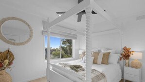 Un lit à baldaquin blanc donnant sur l’extérieur, un miroir rond et une table de chevet avec une lampe.