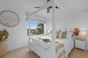 Ein weißes Himmelbett mit Blick ins Freie, ein runder Spiegel und ein Nachttisch mit Lampe.