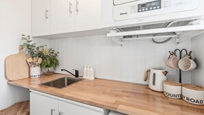 Une cuisine avec des armoires blanches, un plan de travail en bois, un évier, une machine à café et un étagère suspendue où sont rangées des casseroles et des poêles.