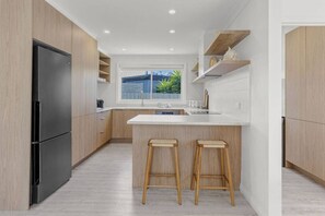 A modern kitchen with a black refrigerator, wooden cabinets, a white countertop, and two wooden stools. - Coastal Waters - Spa, Sleeps 8, Newly Renovated (499538) (Ocean Grove)